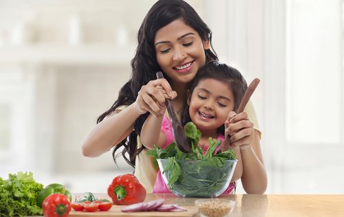 Mother and young daughter mixing a fresh spinach salad together in the kitchen